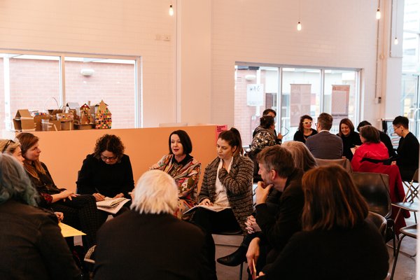 A group of adults sit on chair in a circle engaged in discussion.