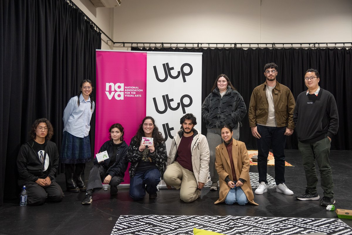 Photo of a group of people standing and sitting in row, they are smiling and some of them are holding NAVA Code of Practice postcards. Behind them are two pull up banners, one is pink and features the NAVA logo, one is white with the Utp logo in black