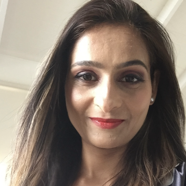 Headshot of Anjli Punia. She has long brown hair, wearing red lipstick. She is smiling and looking down into camera.