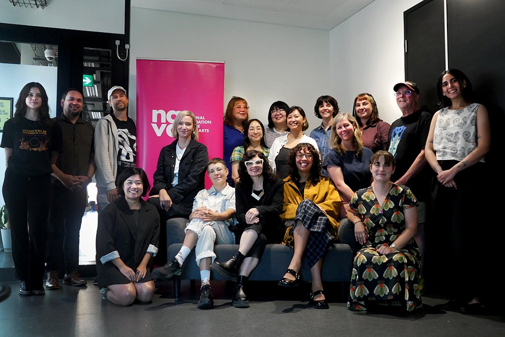 Photo of a large group of people standing and sitting amongst a pink pull up banner with the NAVA logo