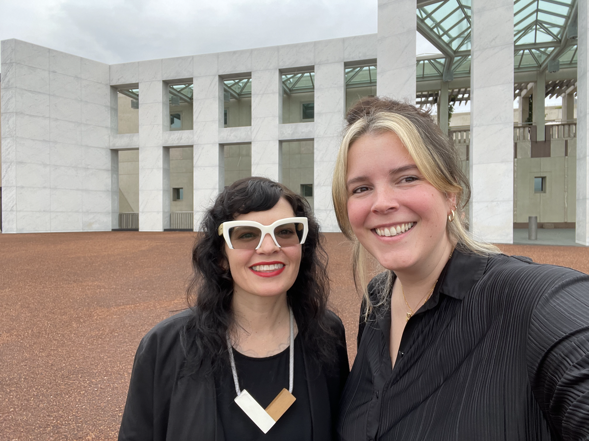 Candid photo of 2 people in front of Parliament House, Canberra. They are wearing black and smiling at the camera.