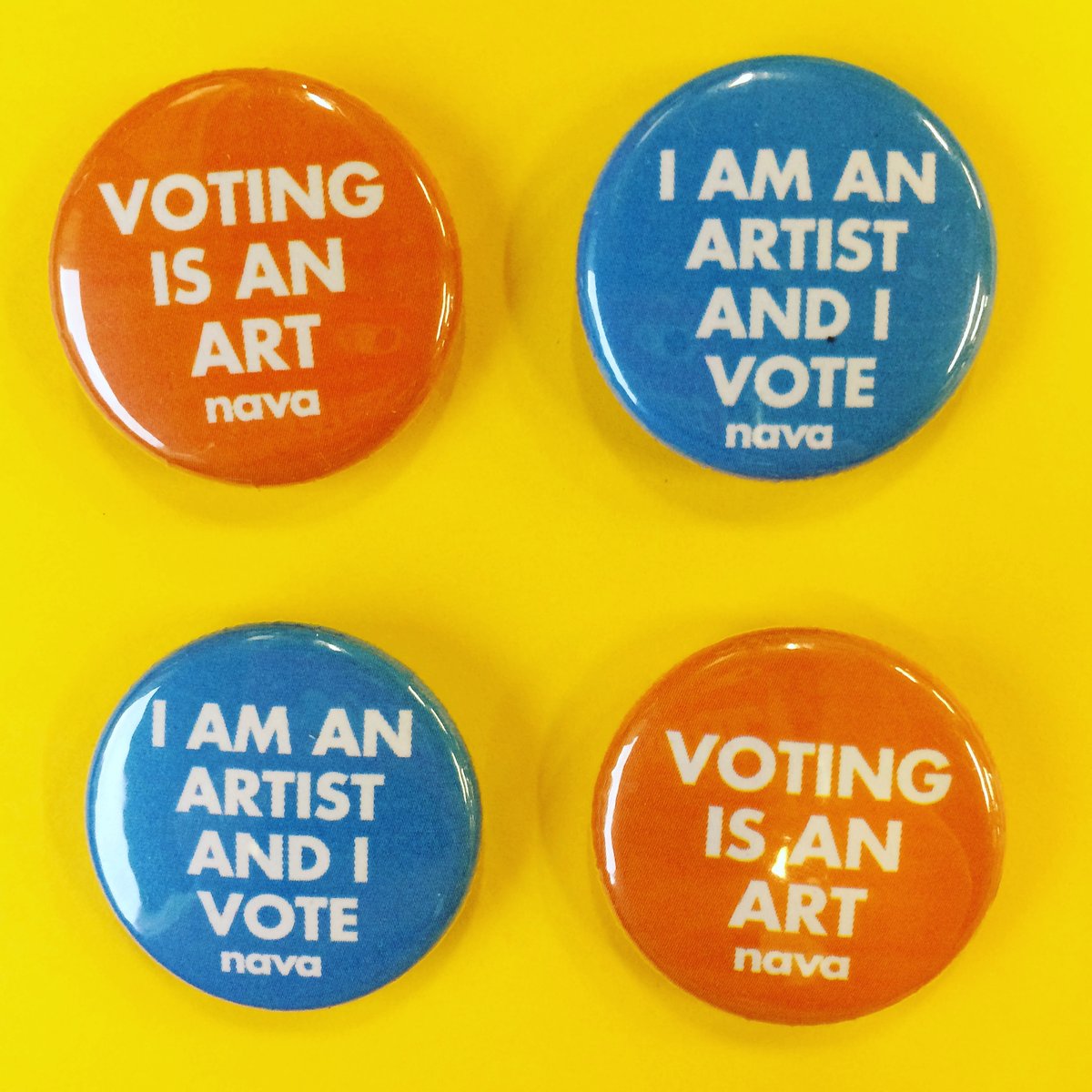 Four badges, two orange with the text in white 'Voting is an art' and two blue with text in white 'I am an artist and I vote' on a yellow background.