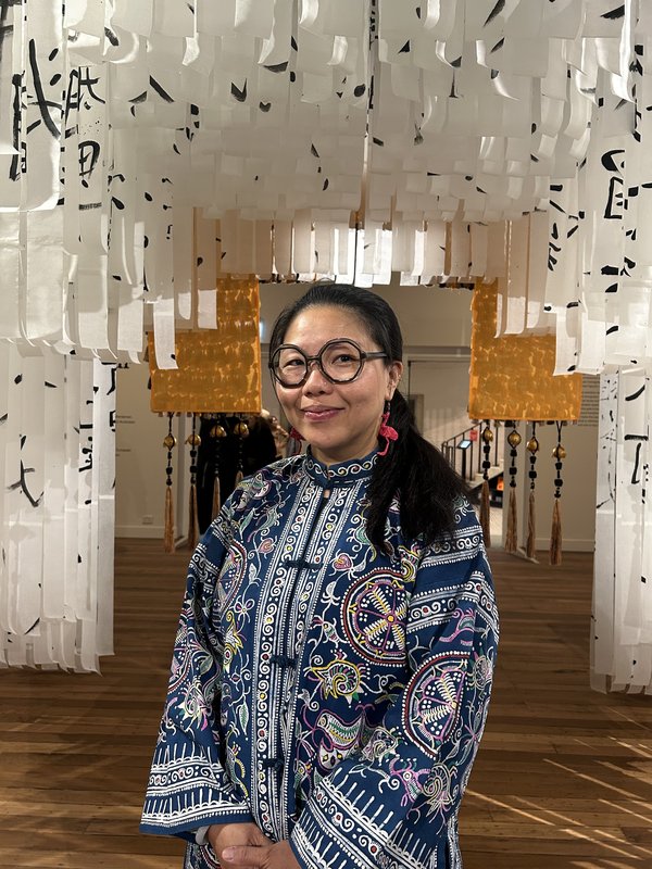 Photo of Jacky standing underneath her installation artwork of long paper strips.