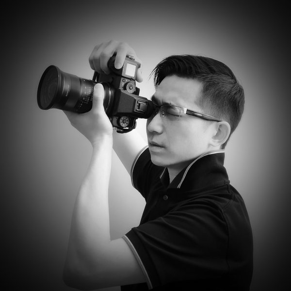 Black and white image of a man wearing glasses and holding a camera to his eye