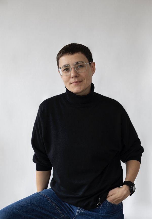 Portrait of Ju wearing a black top, wearing spectacles and has one hand in their poket
