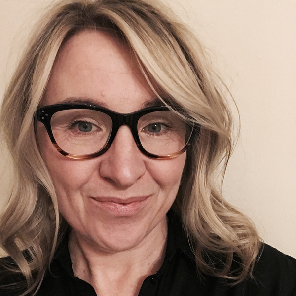 Headshot of Kate Joannou. She is wearing dark framed glasses, has blonde shoulder length hair and is smiling at the camera.