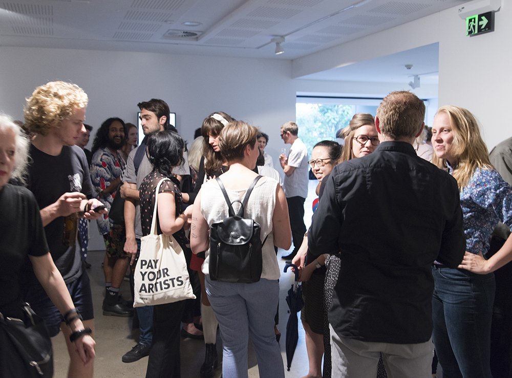 Photo of people standing and chatting at an event in an art gallery spacw.