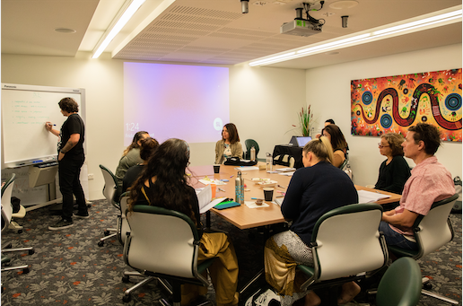 Group of people around a desk with one person writing on a whiteboard.