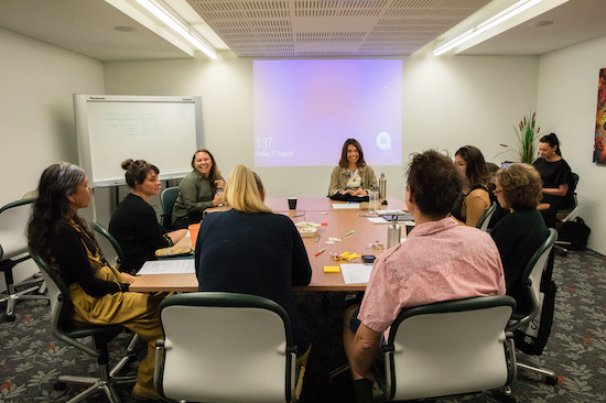 A group of people around a desk with a presentation projected on to a wall in the background.