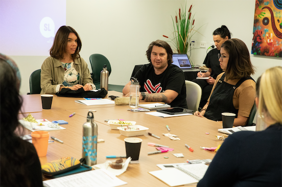 A close up of people sitting around a desk with one person talking with others listening.