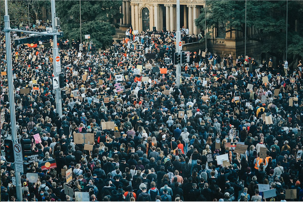 Large group of people protesting in the street holding signs facing towards people giving speeches.