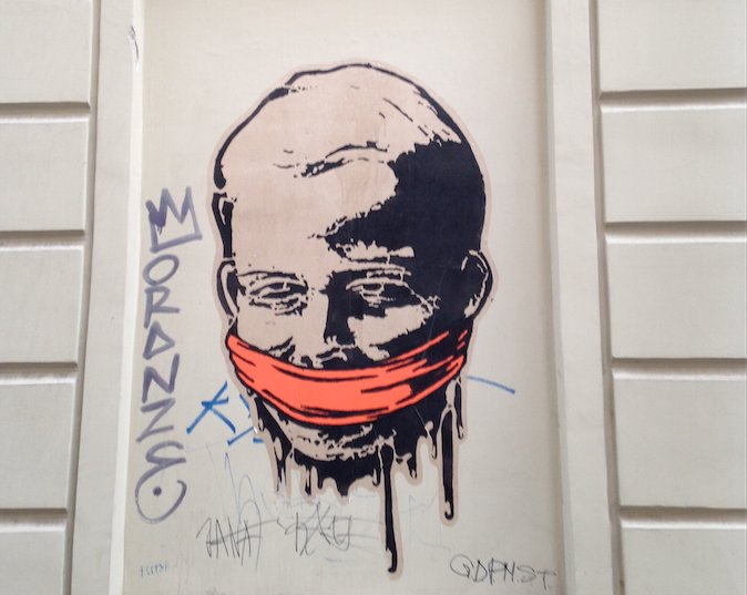A paste up on a wall of a man's head in black and white with a red scarf around his mouth.