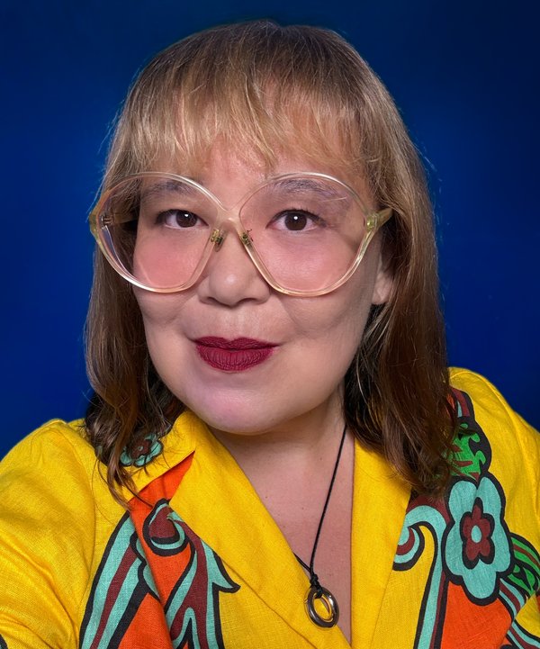 Protrait of Shoufay wearing glasses and a yellow floral shirt with a blue background